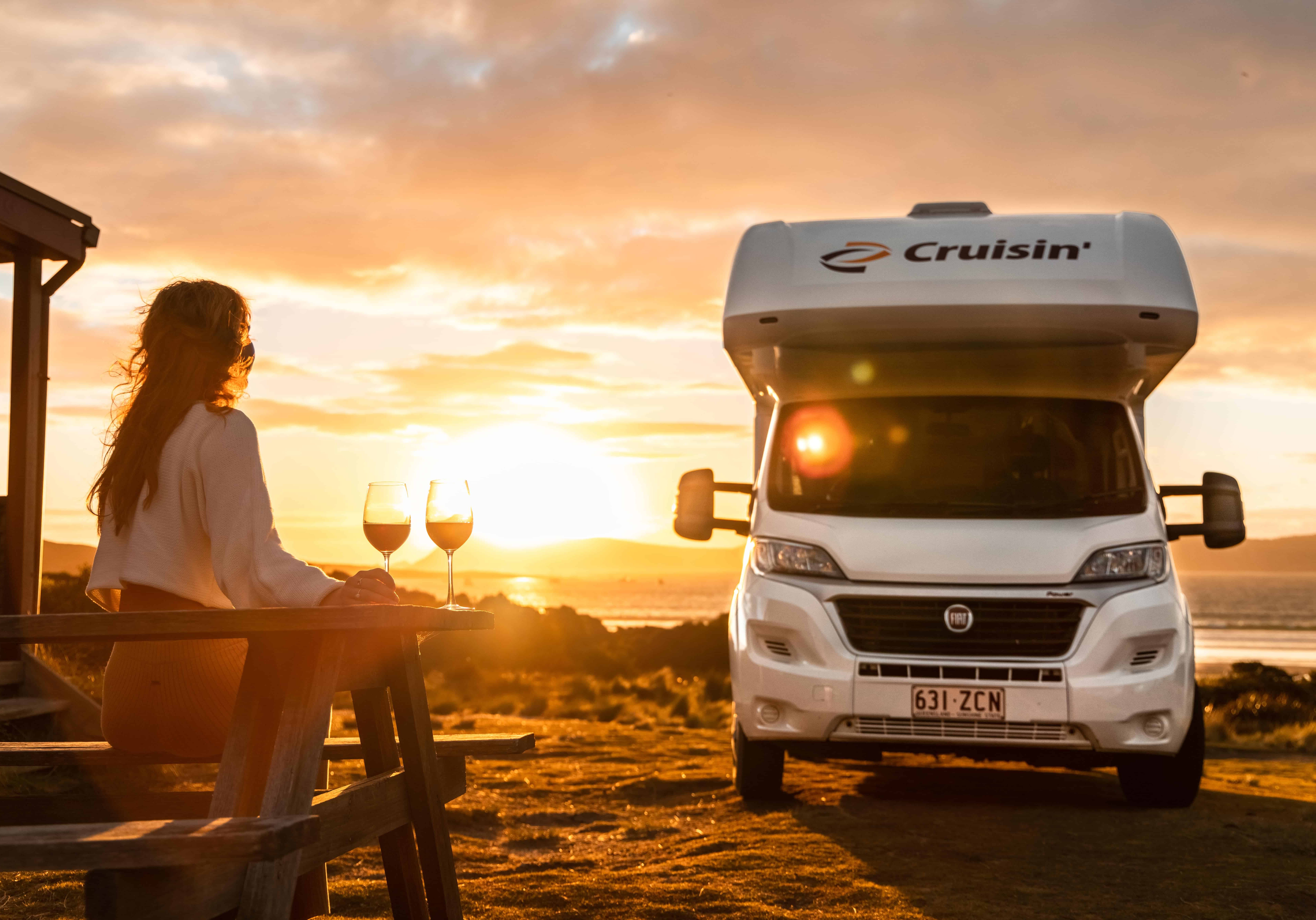Sunset with a woman enjoying wine on outdoor terrace next to a campervan in Australia.
